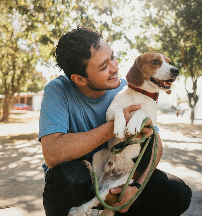 A young man holding his happy dog while they are out on a walk